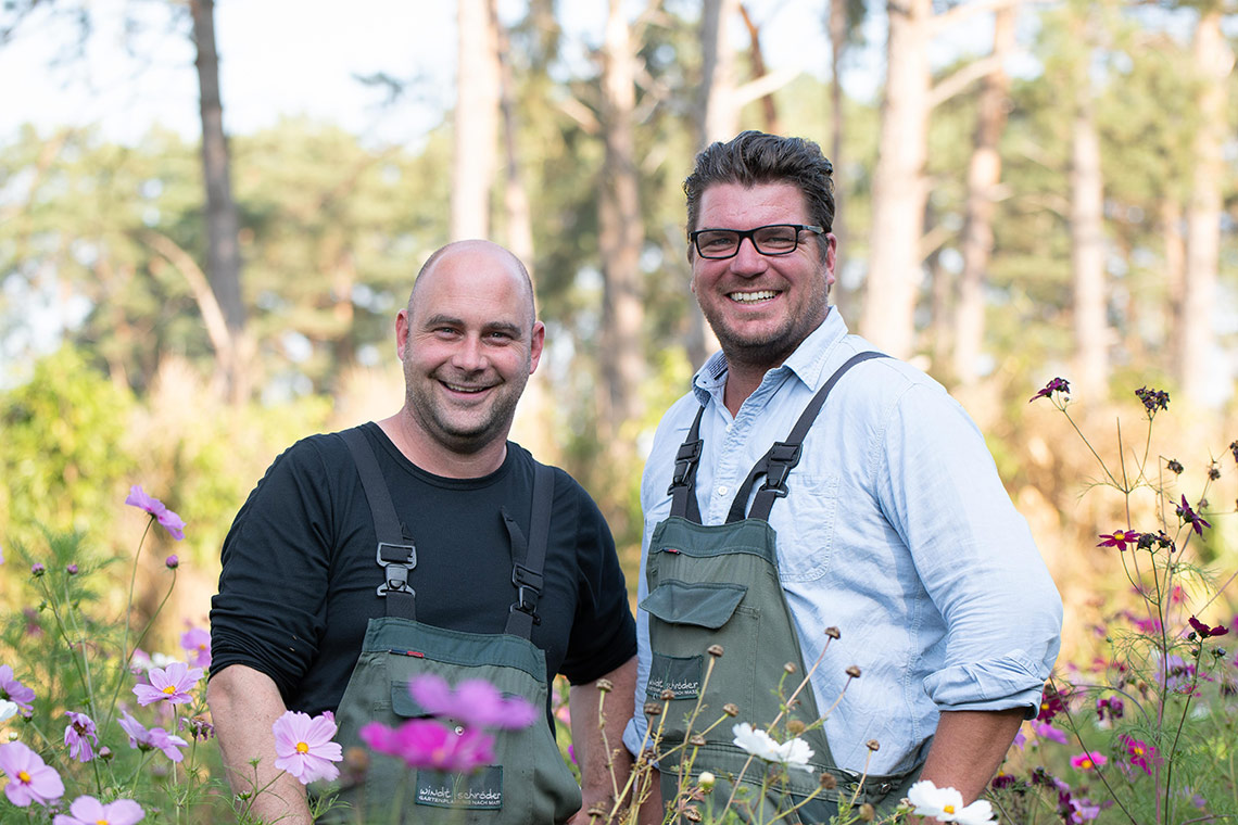 Inhaber gemeinsam in Arbeitskleidung auf einer Blumenwiese: Christian Schröder (links) und André Windt (rechts)
